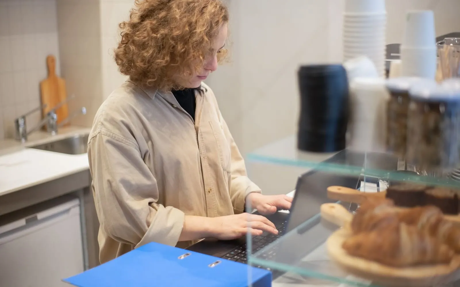 A shop owner working on a laptop behind the counter of a small cafe