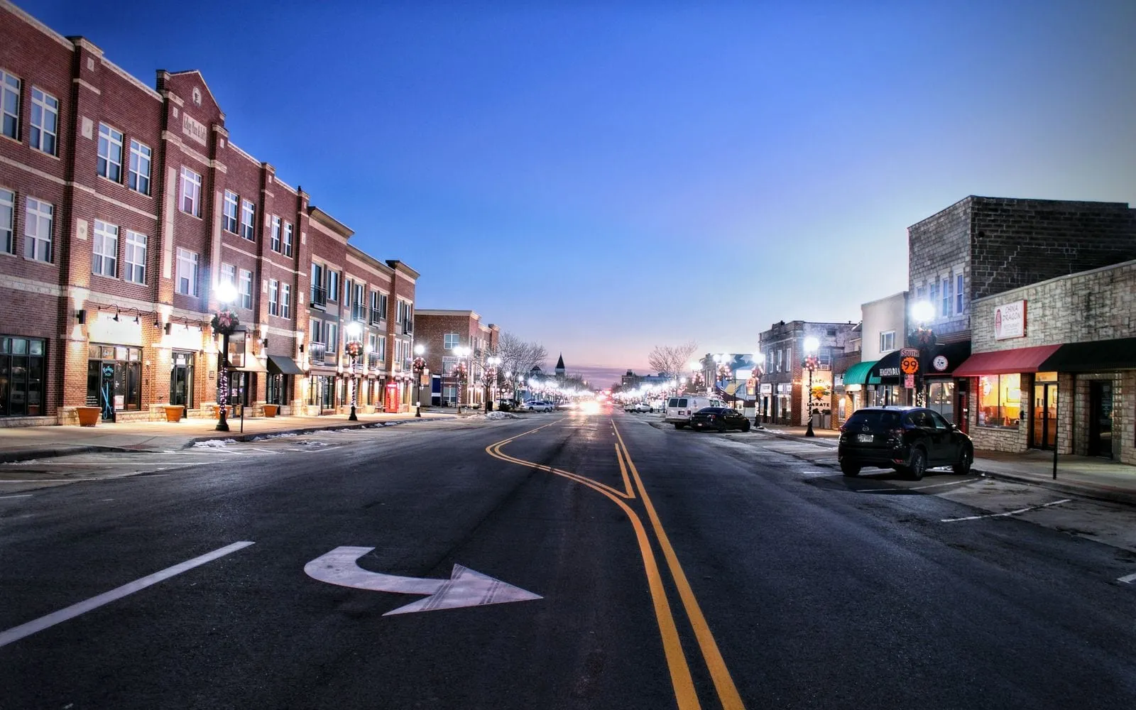 A small-town Main Street at dusk, storefront lights on